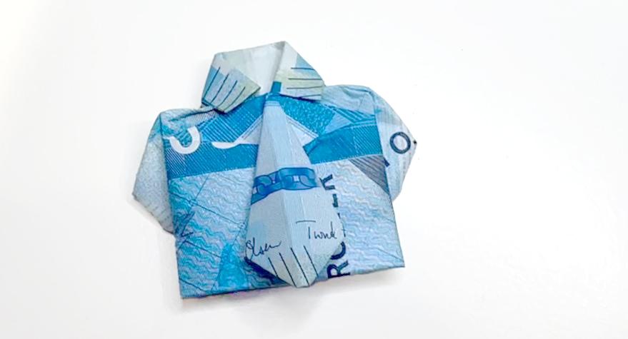 Bildet viser en norsk 200-kronersseddel som er kunstferdig brettet til å ligne en skjorte med slips. Den blågrønne seddelen er nøye formet for å vise kragen, ermene, og et lite slips i midten, som gir inntrykk av et komplett antrekk i miniatyr. Denne kreative brettingen gjør pengegaven både personlig og elegant, og gir et unikt preg til en ellers tradisjonell gave. Detaljene på seddelen fremhever designet, noe som gjør skjorten både gjenkjennelig som en pengeseddel og imponerende som et håndlaget kunstverk.