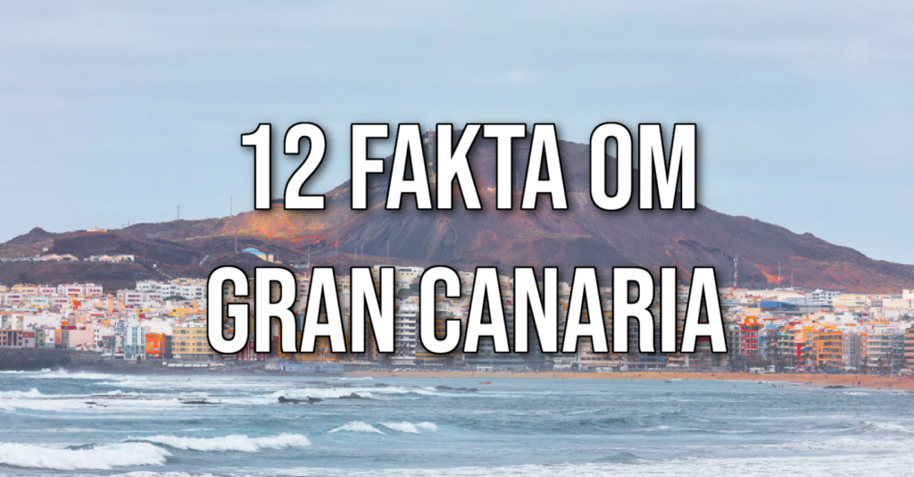 Bildet viser et kystlandskap på Gran Canaria med en by i forgrunnen og en vulkansk bakgrunn i horisonten. Byen har fargerike bygninger som ligger nær stranden, og havet i forgrunnen har små bølger som bryter mot land. Over bildet står teksten "12 fakta om Gran Canaria" skrevet med store, tydelige bokstaver.