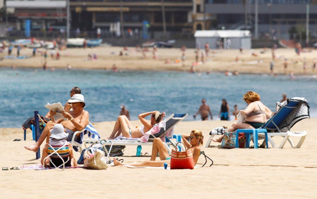 Bilde av turister som soler seg på en strand i Gran Canaria. På bilde ser vi en hvit strand med blått hav i bakgrunn