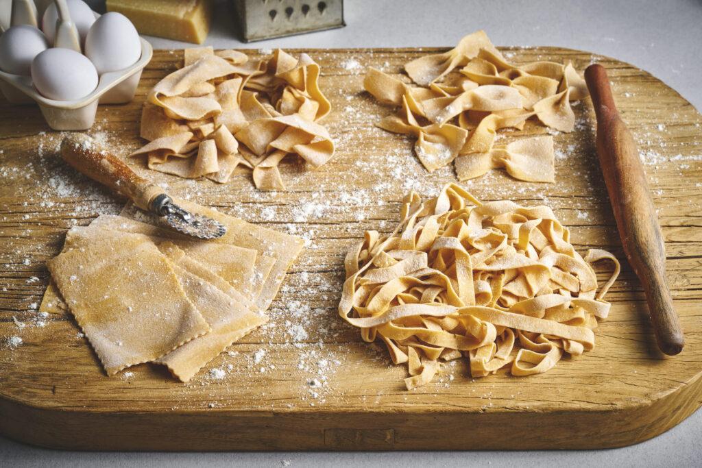 Fire ulike hjemmelagede pasta på en brødfjøl med litt mel og noen egg rundt.