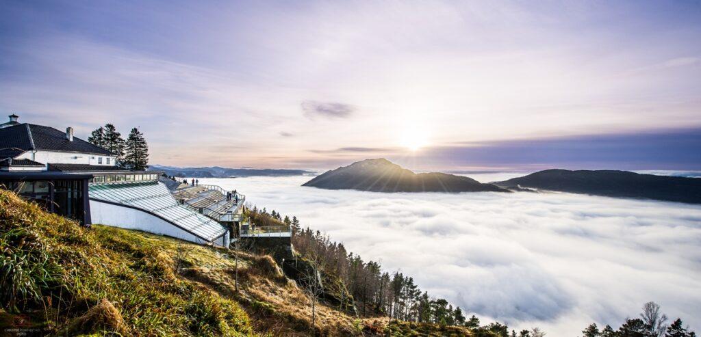 På toppen av Fløyfjellet, over skyene, med utsikt til glassbygg og fjell.