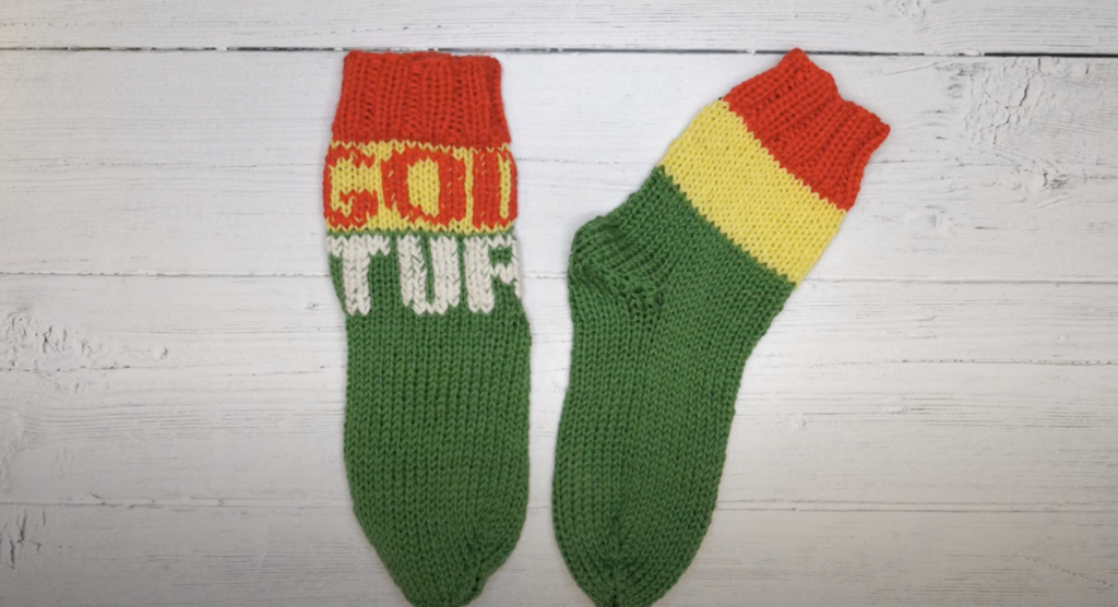 Ferdig resultat av kvikk lunsj sokkene fra strikkeoppskriften, i grøn, gul og rld med teksten "god tur". 