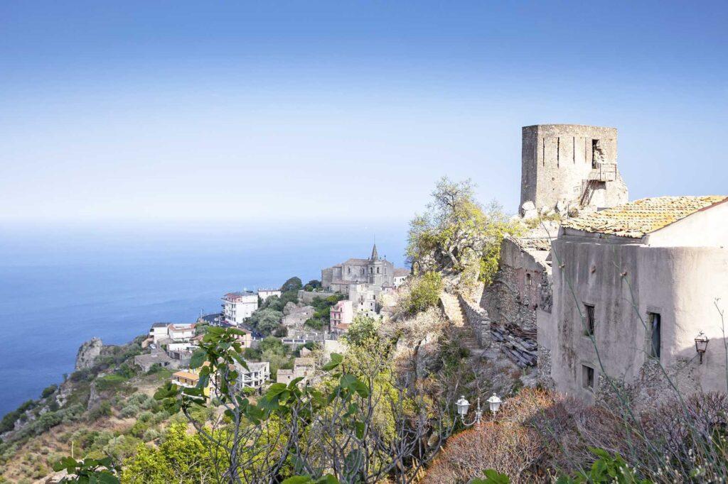 Borg ogbebyggelse ned en ås på Sicilia, med hav og blå himmel i bakgrunn.