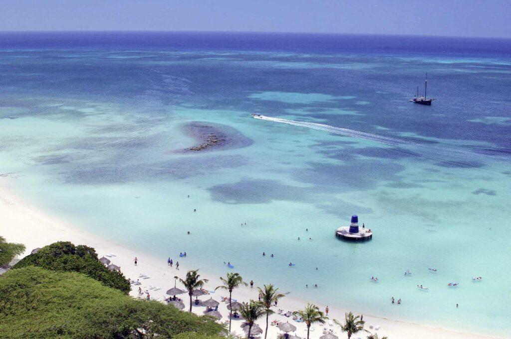 Aruba, drømmesommerferien med kritthvit strand og blått hav, med folk som bader og båt.