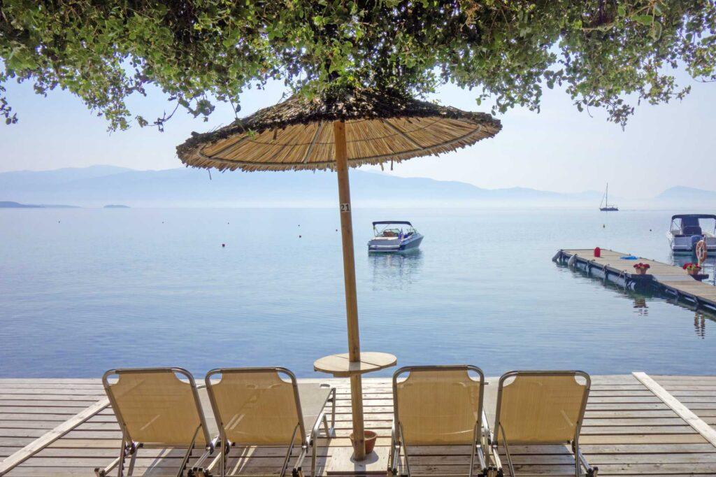 Bilde fra sommerferie i syden på greske Lefkas. Solsenger og parasoller med utsikt til havet og båt.