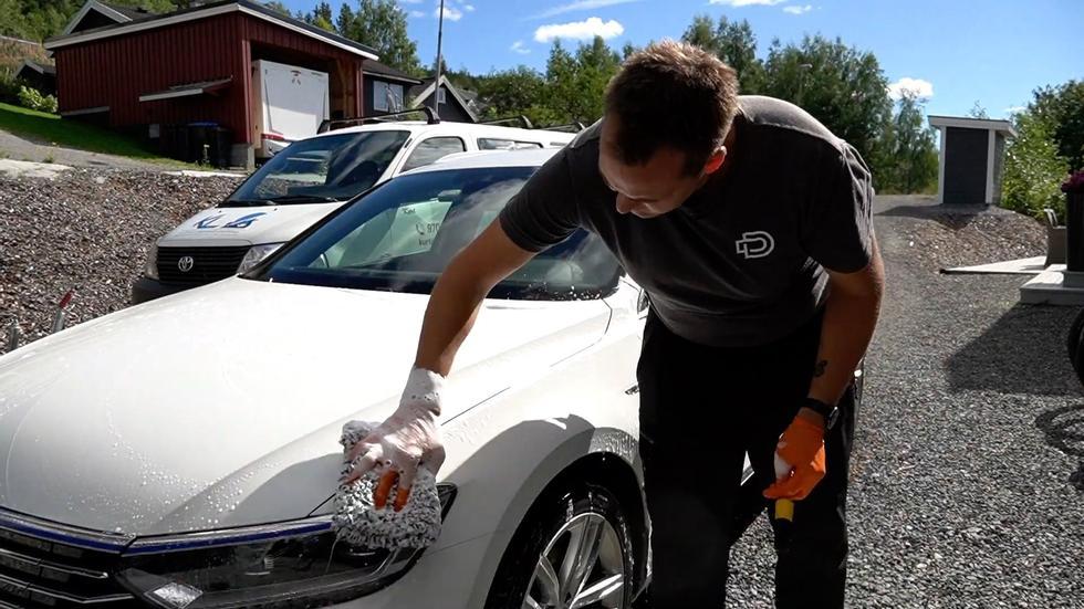 Mann som driver med bilvask og vasker fronten på bilen med en vaskepad av mikrofiber