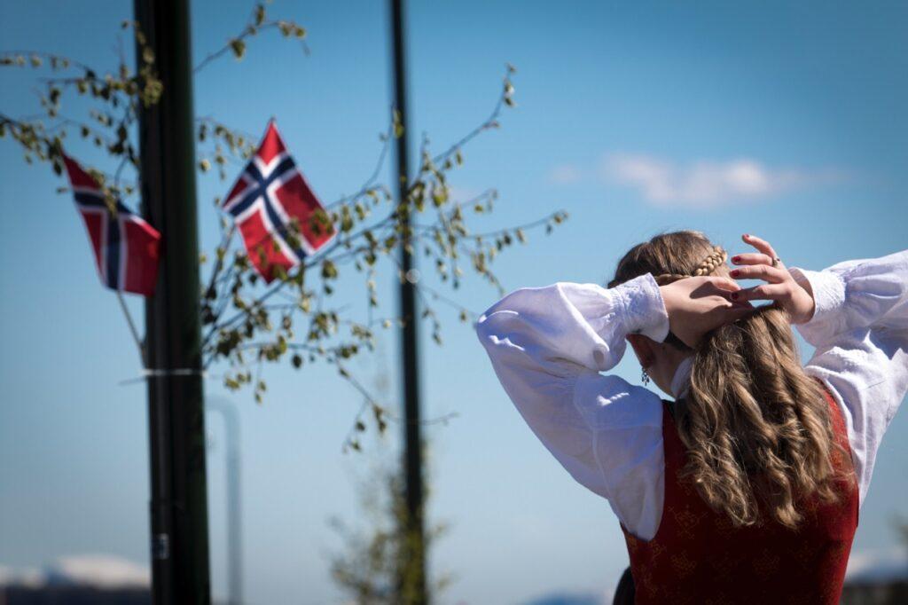 Bilde av jente i bunad foran lyktestolpe med norske flagg på 17. mai.