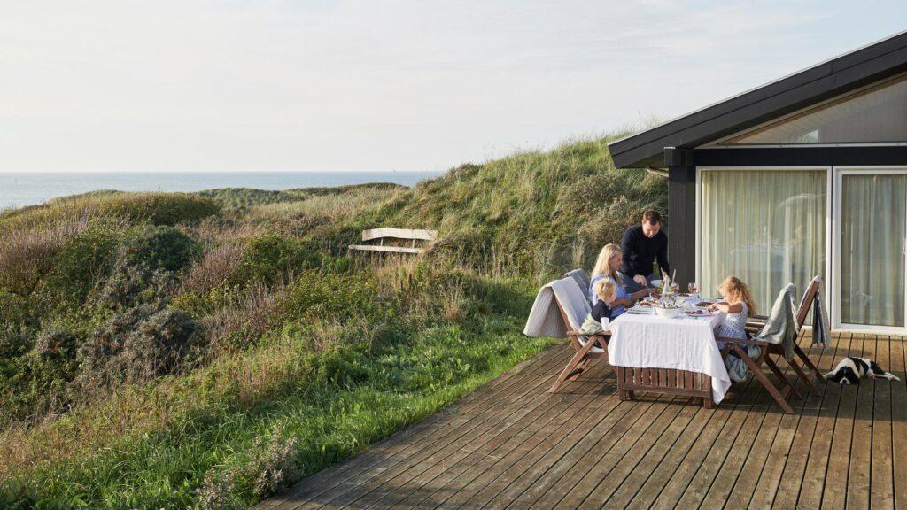 feriehus i danmark familie på fire som spiser på terrassen nær sjøen.