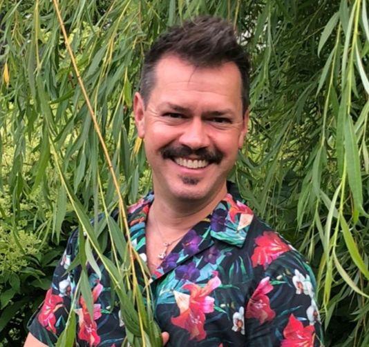 Bilde av Espen Skarphagen med stort smil og i i blomstrete skjorte i hagen sin.