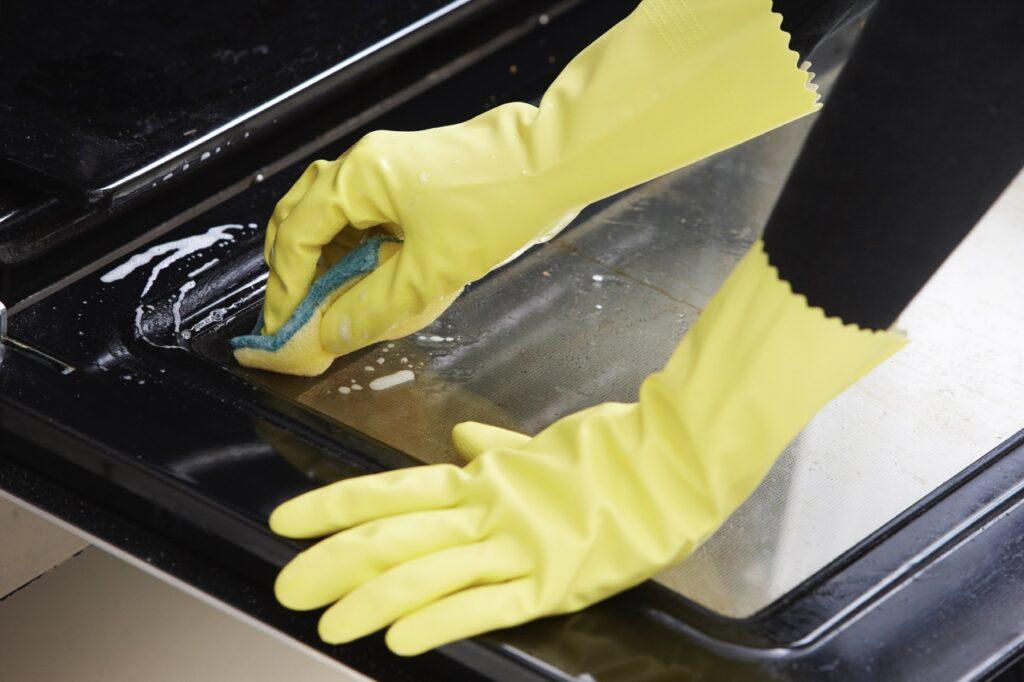 Bilde av hender med vaskehansker som vasker døren på en stekeovn med en gul svamp.