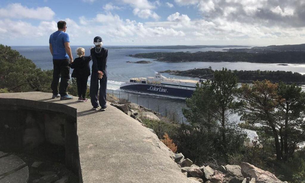 Odderøya i kristiansand to voksne og ett barn som ser på utsikten over kristiansand mens en ferge farer forbi.
