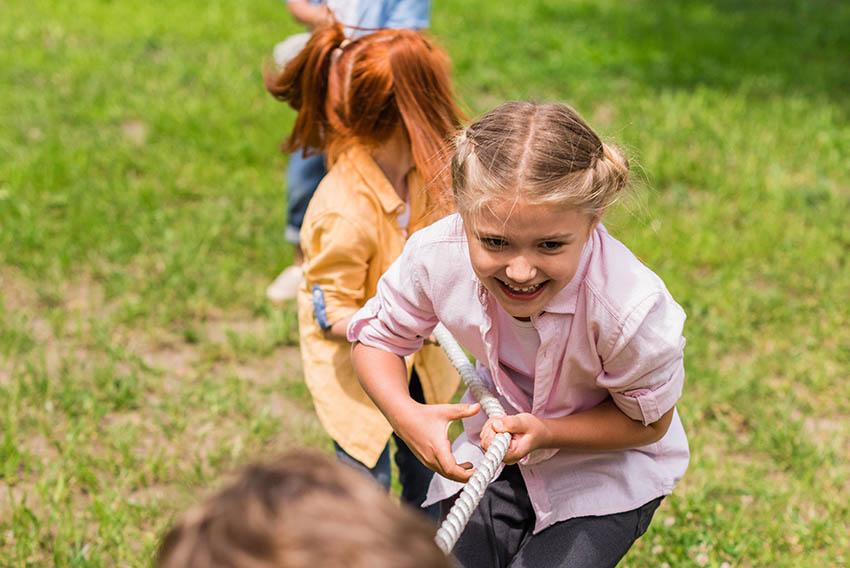 Bilde av barn som leker selskapsleken tautrekking ute i naturen på grønt gress. En perfekt lek til 17. mai.