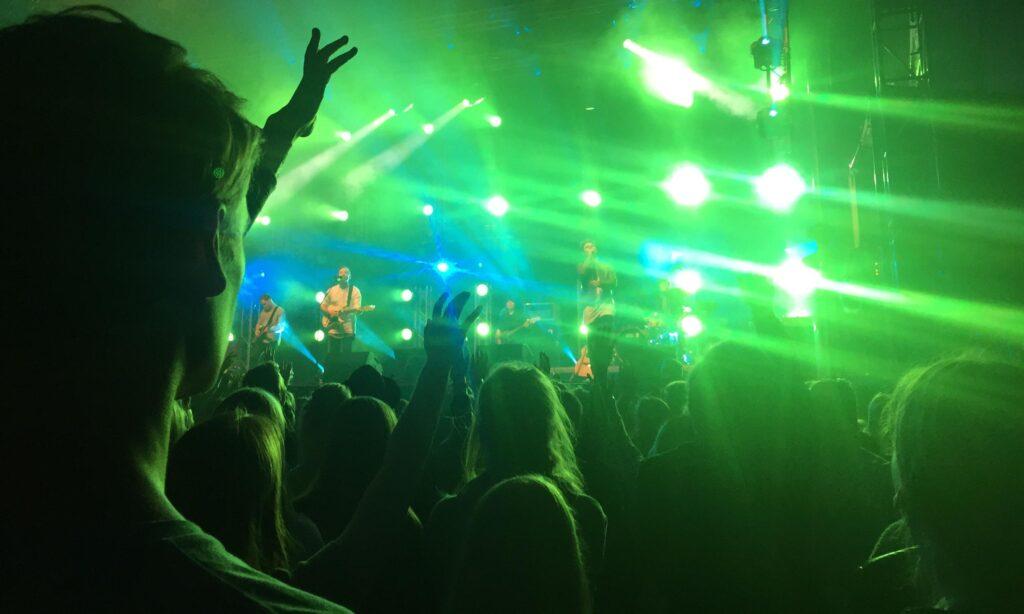 Konsertliv i Oslo, grønne neonlys og personer med hendene i været som danser til musikk fra band på scene i bakgrunnen.