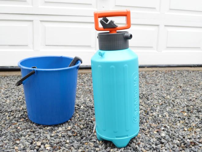Blå bøtte og pumpekanne til såpevann klar for husvask på gårdsplass.