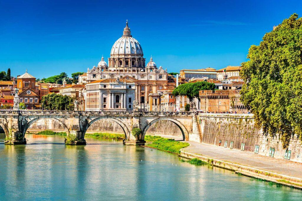 Vatikanet i Roma med sol fra skyfri himmel og gammel bru over elv. 