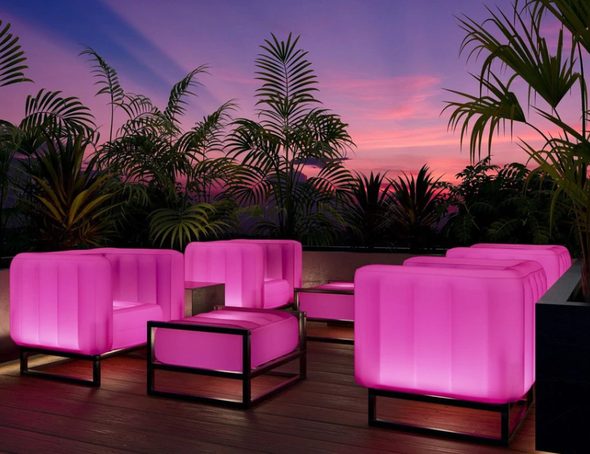 Lysende rosa interiørmøbler i plast med palmer og kveldshimmel i bakgrunnen. 