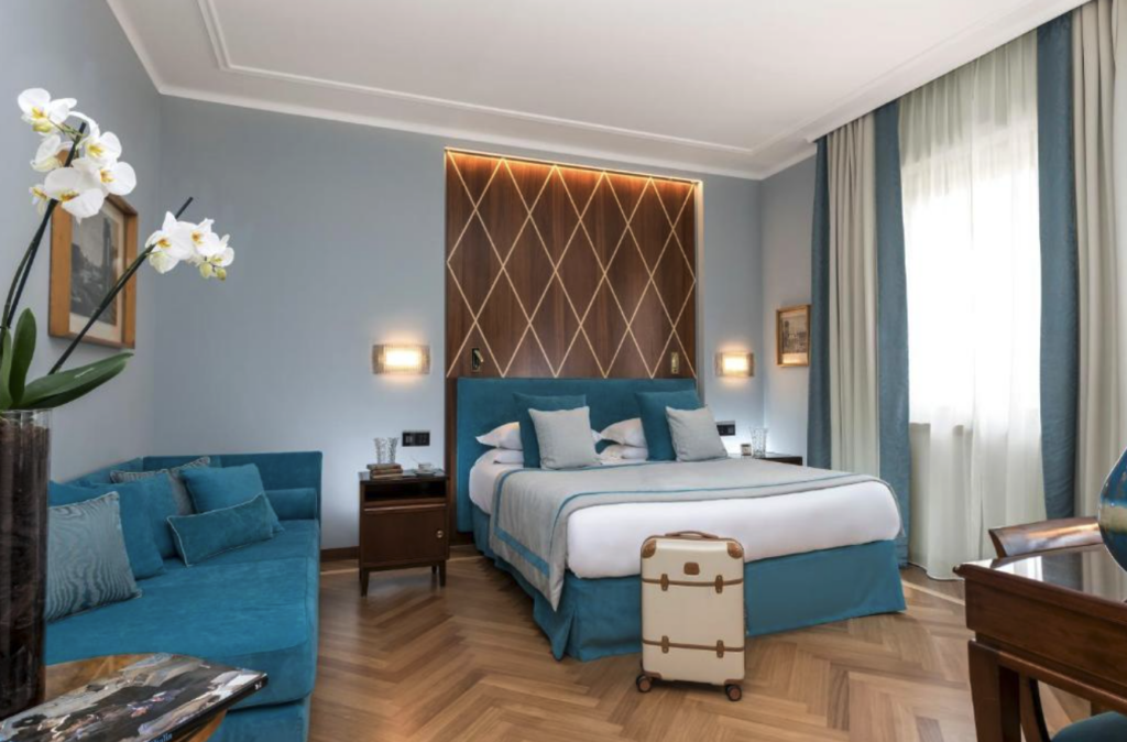 Stort hotellrom med dobbeltseng, blå sofa og lyseblå vegger. 