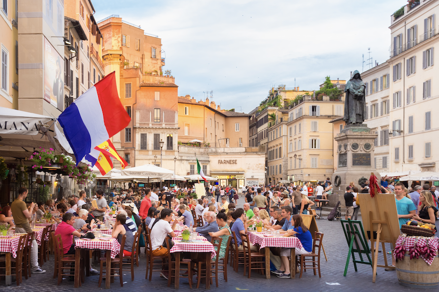 Mange mennesker som spiser på fortausrestaurant i Roma med rødrutete duker. 