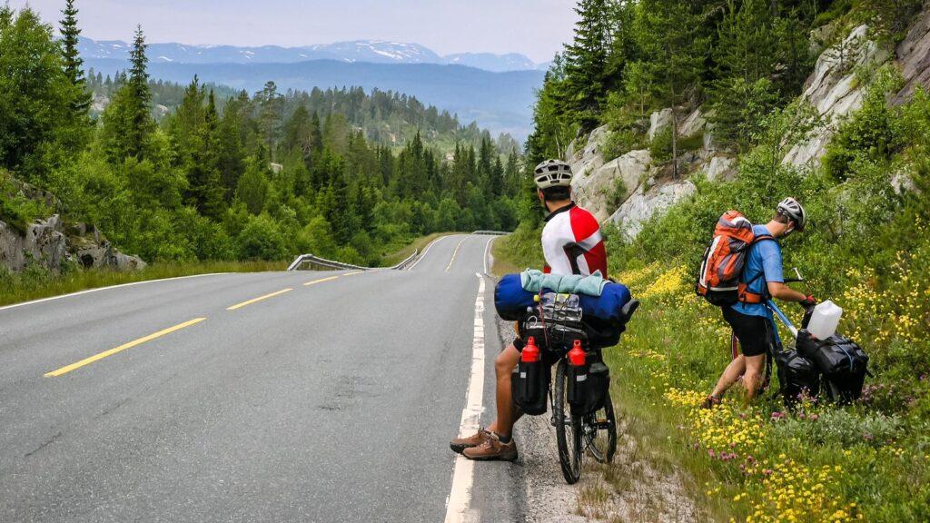 Bilde av to menn ved sykkel langs vei på sykkeltur i vakker natur i Norge. Med sykkelutstyr og hjelm. 