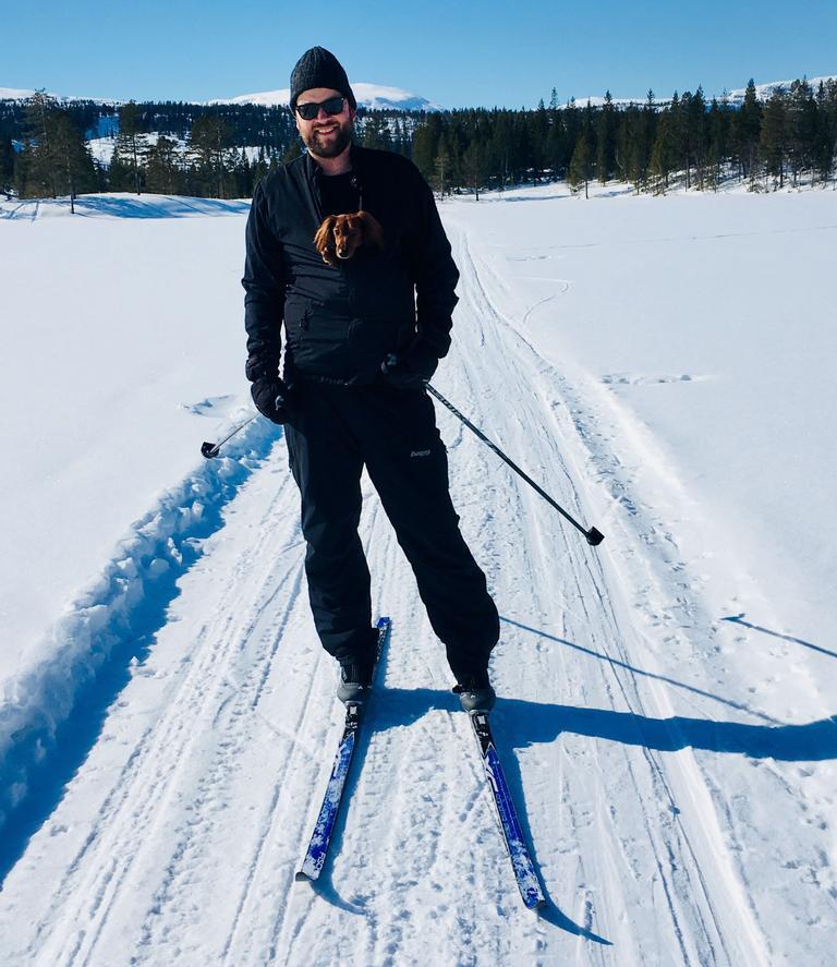Mann på ski med hund i sekk på magen.