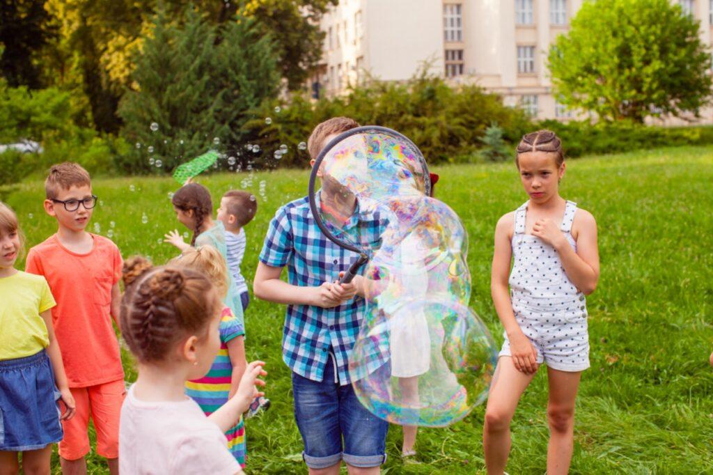 Barn som blåser store såpebobler ute i park.