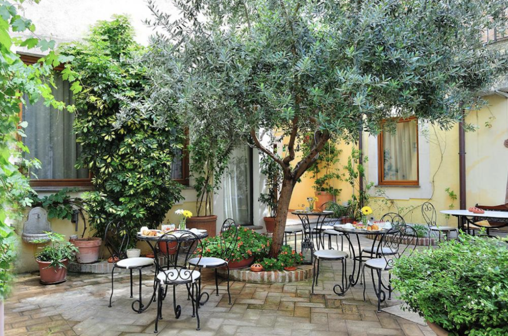 Koselig bakgård med trær og blomster og stoler og bord i Italia