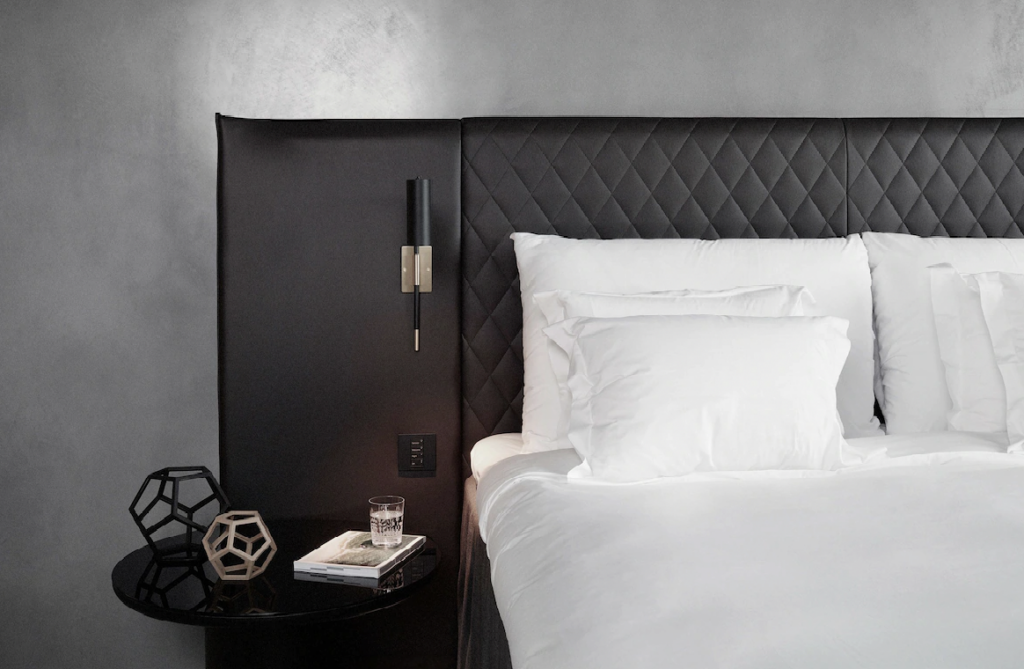 Dobbeltseng med mørk sengegavl i skinn, nattbord og hvitt sengetøy på hotell i Stockholm.