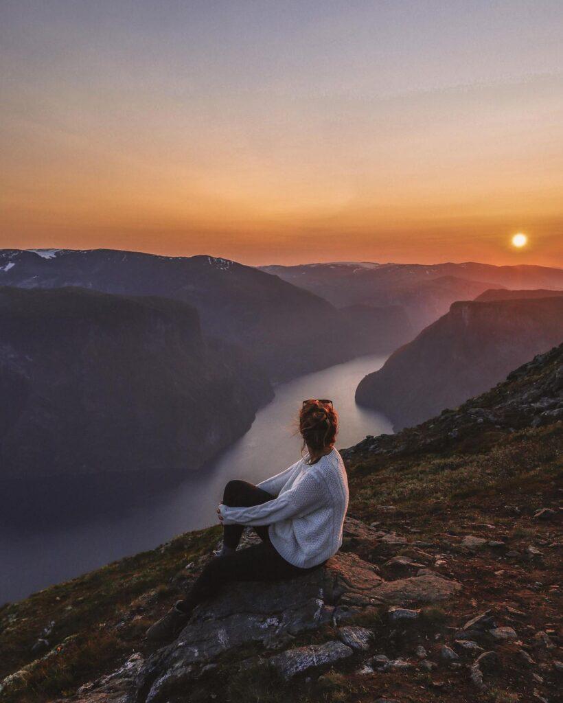 Norgesferie til vestlandet: Bilde av kvinne på topen av fjeld med spektakulær utsikt til Sognefjorden i solnedgang.
