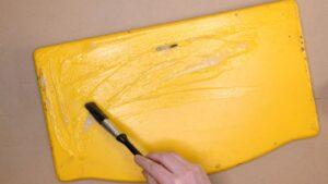 Pensel påfører malingsfjerning på gul tripptrapp-stol.