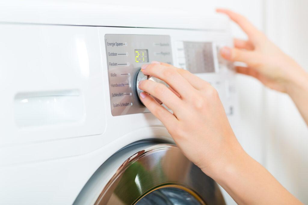 Kvinnehender stiller inn ny vask på vaskemaskin-panel.
