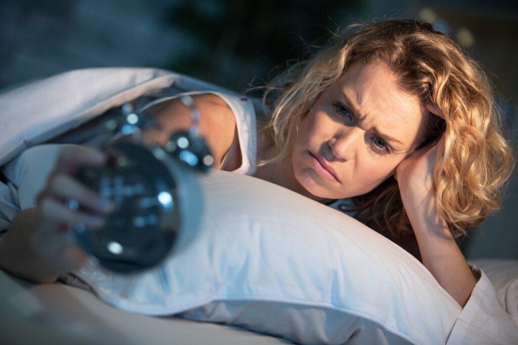 Bilde av kvinne med søvnproblemer i seng med vekkeklokke. 