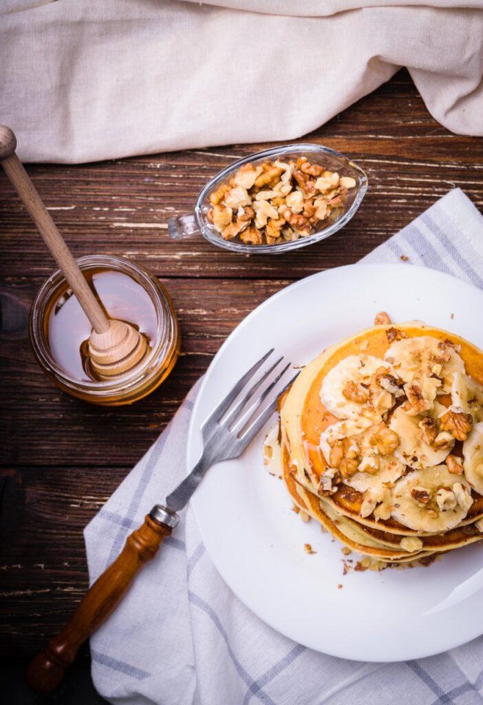 Oppskrift på sunne pannekaker med banan. Bilde av bananpannekaker med honning, valnøtter på bord.