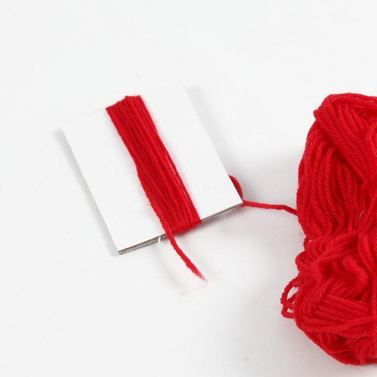 Bilde av rød tråd surret rundt pappbit til strikkeoppskrift nisselue