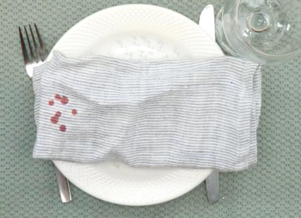 Bilde av rød stearin på tøyserviett på hvit tallerken med vinglass, kniv og gaffel og grønn duk