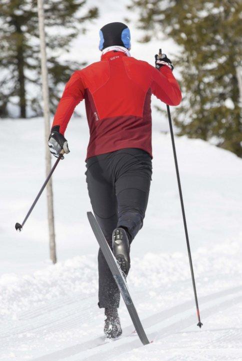 Bilde av mann med rød jakke og sorte skibukser på skitur med langrennski i vinterlandskap med felleski på beina.
