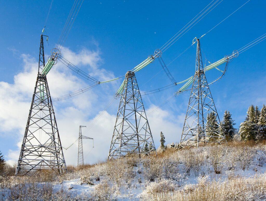 Bilde av tre høyspentledninger ute i naturen med snø på bakken. Vi forklarer hvorfor strømprisene er så høye, varierer og hvordan det spås at de blir fremover. Dette er nemlig faktorene som gjør strømregningen så dyr nå og i 2023. 