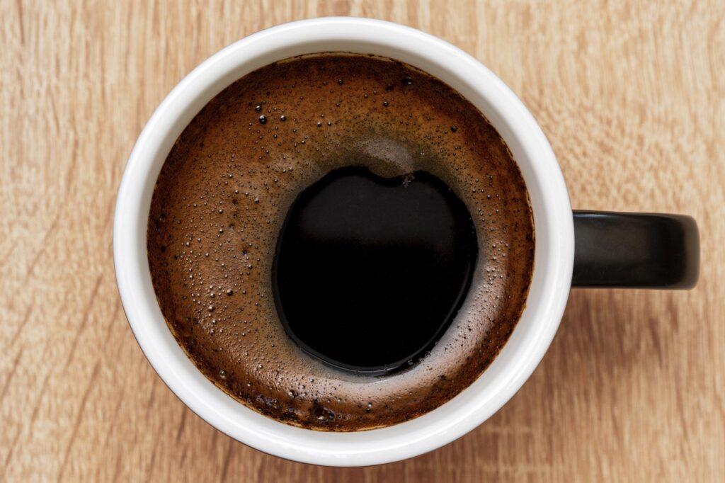 Bilde av en sort og hvit keramikk-kopp med sort kaffe på trebord.