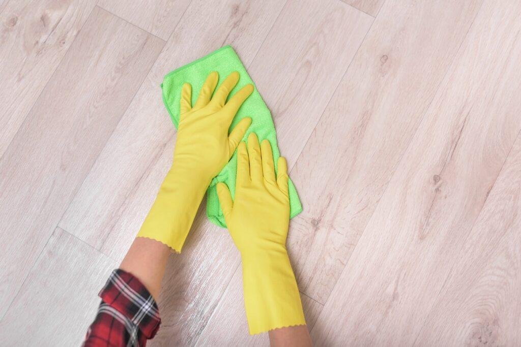 Bilde av hender med gule oppvaskhansker som holder en grønn mikrofiberklut og vasker gulv