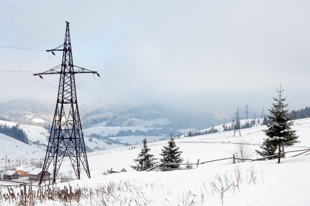 Bilde av mast med høyspentledninger i snødekket landskap til sak om strømpriser og hvorvidt det er spotpris, fastpris og variabel strømavtale, hvilken som lønner seg og er billigst. Dette er det lurt å vite svaret på om strømregningen din er dyr i år!