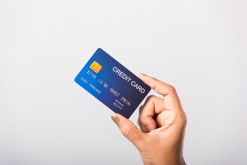 Hånd som holder opp et blått kredittkort mot hvit bakgrund. Vi har funnet de beste kredittkortene til forskjellig bruk.