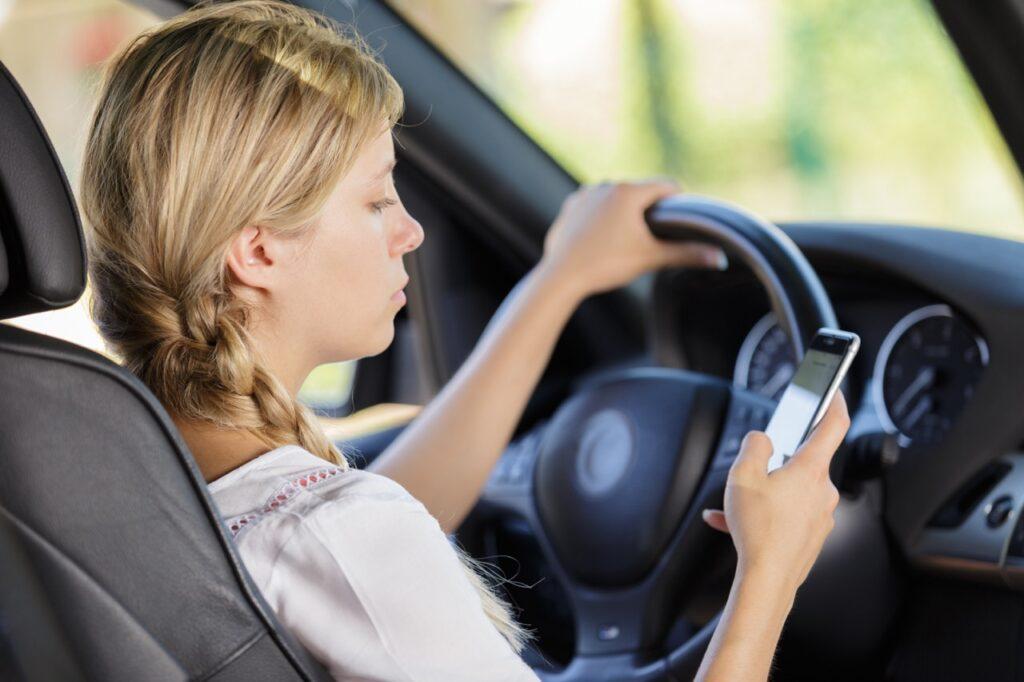 Kvinne med lyst hår som bruker mobilen mens hun kjører bil. Her får du oversikt over bøtesatsene for fart, mobilbruk og promille.