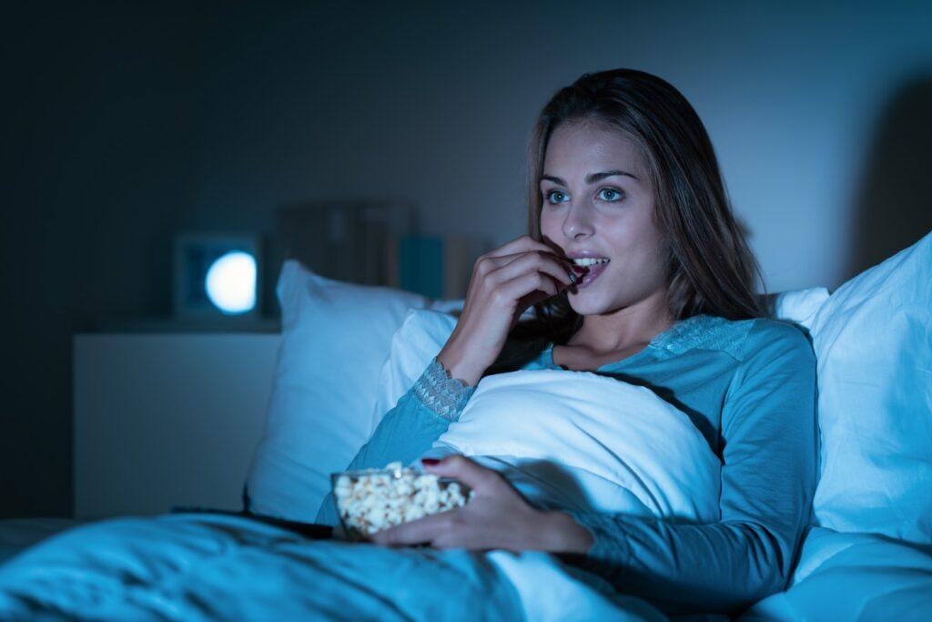 Mini-projektor test: En kvinne spiser popcorn i senga mens hun ser på film.