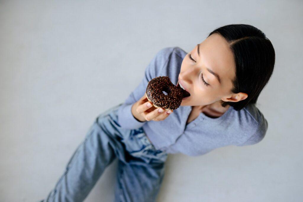 Bilde av kvinne som skal til å ta seg en bit av en donut dekket av sjokolade til artikkelen som forklarer hvorfor noen mennesker aldri legger på seg. Er det egentlig fordi de har høyere forbrenning, eller kanskje fordi de spiser færre kalorier? Vi forklarer den overraskende sannheten. 