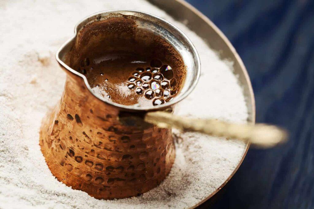 Bilde av verdens sunneste kaffe, gres kaffe i en briki/ibrik/tyrkisk/gresk kaffekanne på et fat med sand. Kaffeen med «crema» eller skum på toppen. Her får du oppskriften.