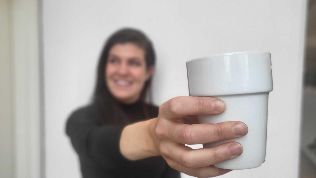 Bilde av kvinne med hvit kaffekopp i handen til saken som gir deg svaret på hvorvidt det er lurt å drikke kaffe på tom mage eller ei.