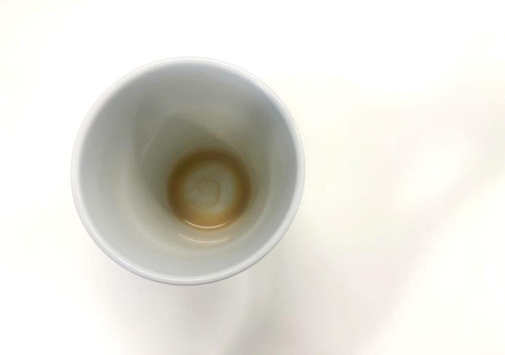 Bilde av tom kaffekopp på hvitt bord til artikkel som gir deg svaret på om det er lurt å drikke kaffe på tom mage. 
