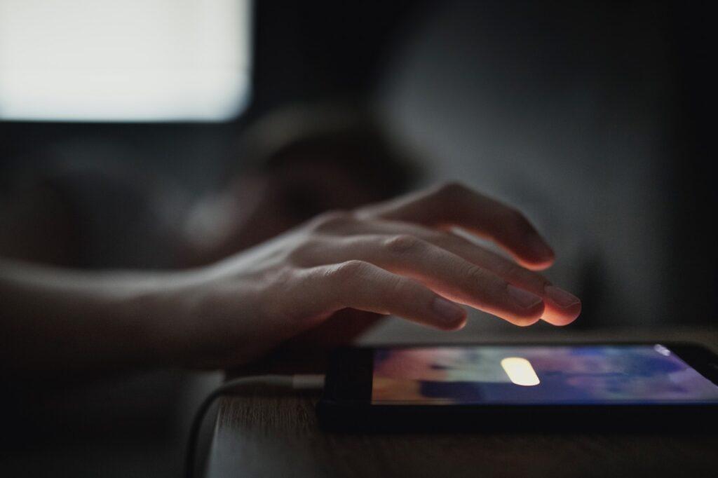 Bilde av handen til en person i seng som trykker på «snooze»-knappen og snoozer» nor forskning og ekspertene ikke anbefaler. 