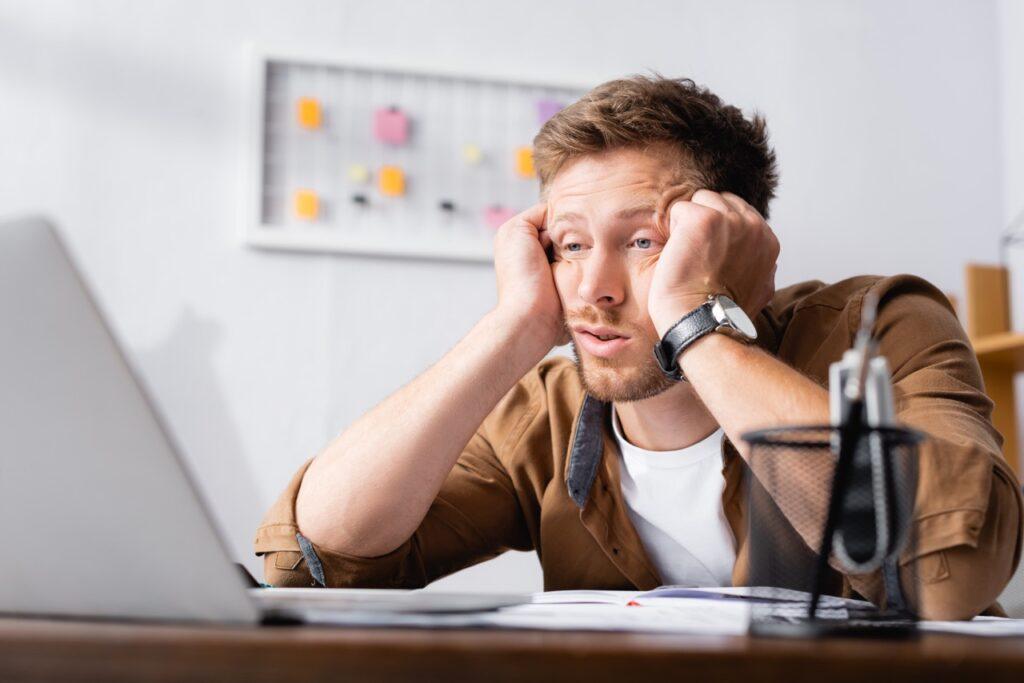 Bilde av mann som er søvnig på jobb og som sitter ved en pult foran en pc. Vi forteller hvorfor du ikke bør snooze eller trykke på snooze-knappen.