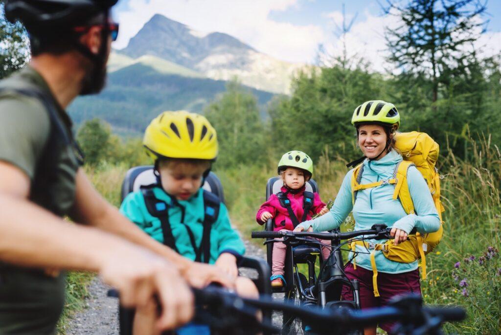 Familie på sykkeltur, mor og far har hvert sitt barn som passasjer på sykkelen. Vi forteller deg reglene du må kunne når du skal ha passasjerer på sykkelen.