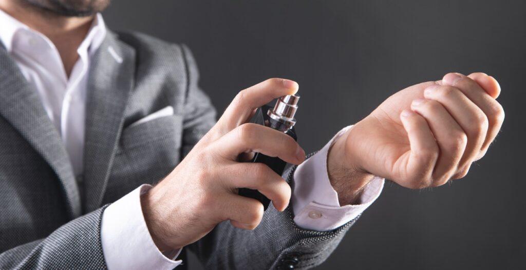 Nærbilde av mann som i grå dress som sprayer parfyme på håndleddet. Vi har samlet de mest populære parfymene til herre, velg blant Armani, Versace, ysl, Hugo Boss og Dior.